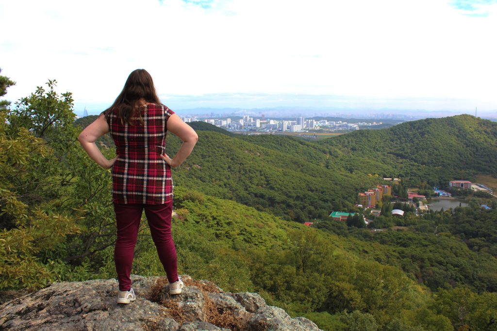 Photo of myself standing on a rock overlooking the view of Pyongyang in the distance