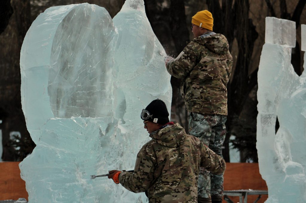 Two men working on carving an ice sculpture