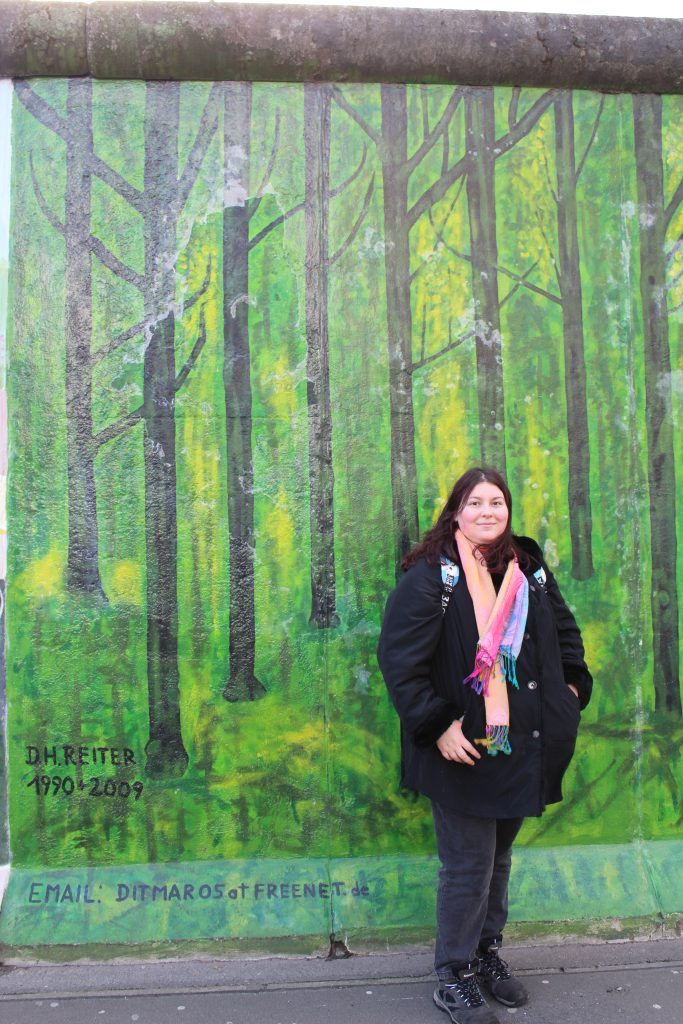 Photo of myself standing in front of a forest mural at the East Side Gallery
