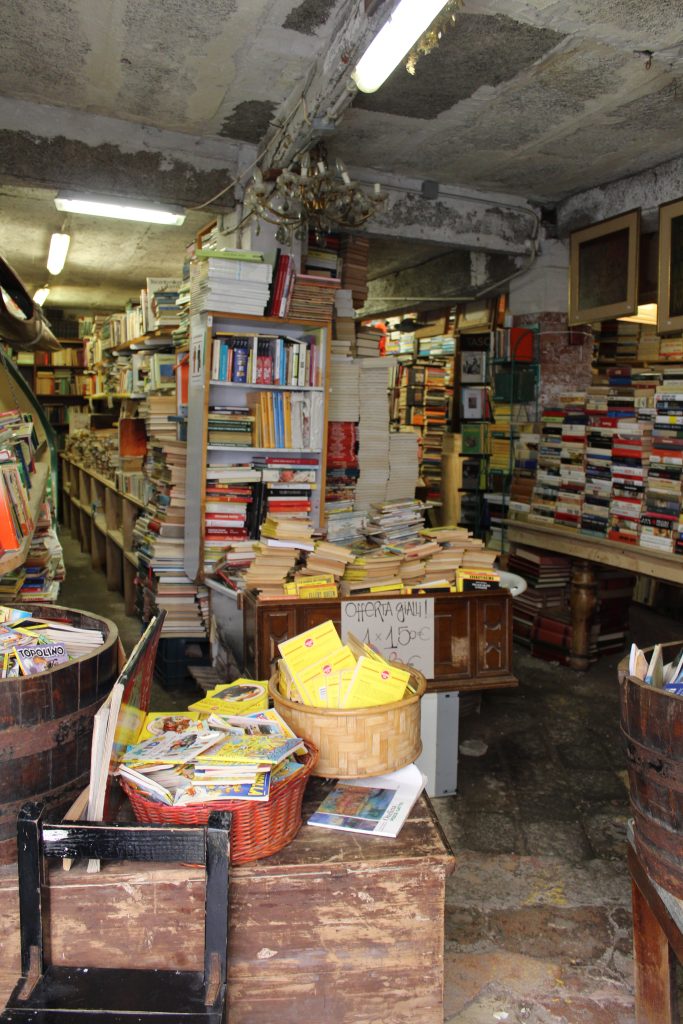 Photo of the inside of Libreria Acqua Alta showing different containers used to store books such as baskets and a barrel.