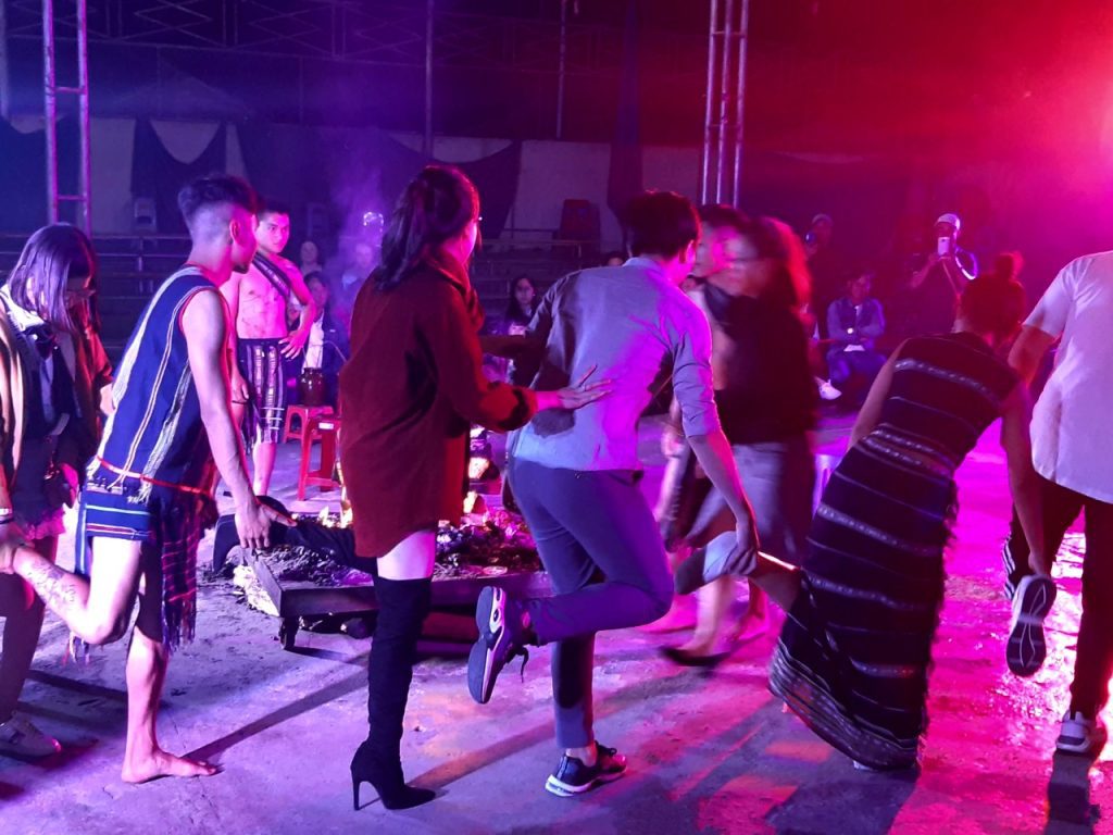 Photo of a group of people dancing in a circle, each holding the the foot of the person in front of them.