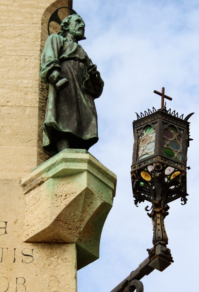 Photo of a statue of San Marino next to a lamp post with many different coloured circles of glass.
