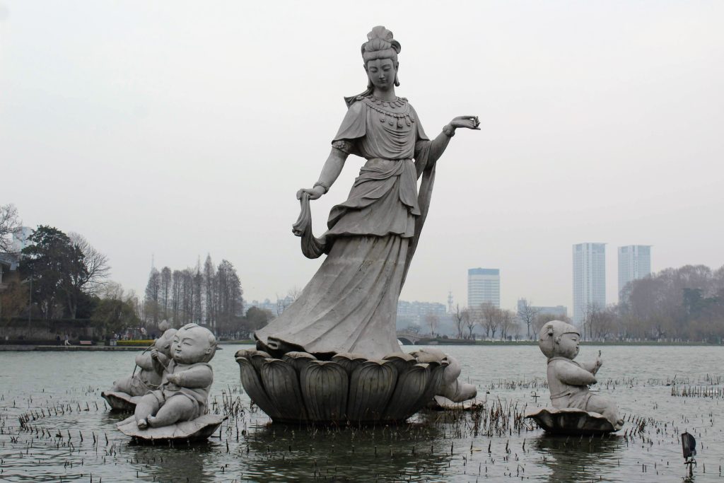 Photo of sculpture of a woman surrounded by several small sculptures of babies in the middle of a lake.