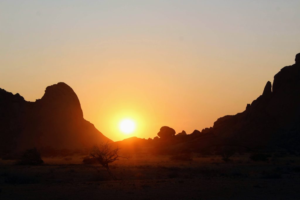 Photo of the sun setting between various peaks of Spitzkoppe