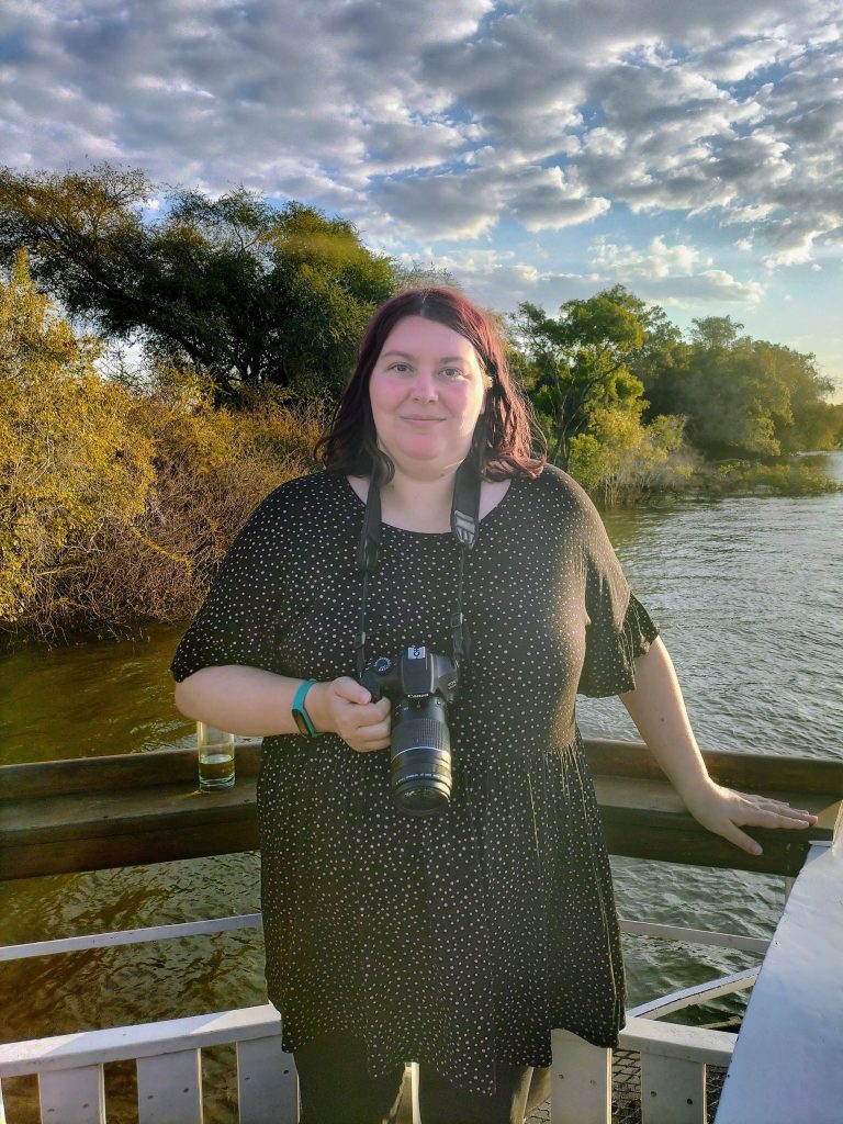 Photo of me with a camera around my neck, standing at the railing of the boat.