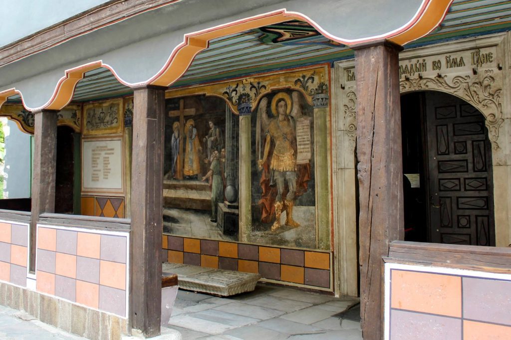 Photo of the outside of a church. The walls are beautifully painted with religious images.
