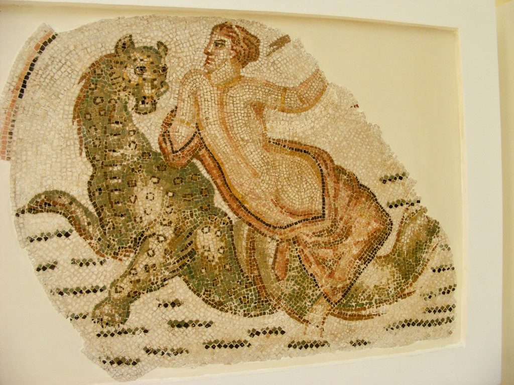 Mosaic of a naked woman riding a strange looking beast. It is green with a feline shape and lots of spots.