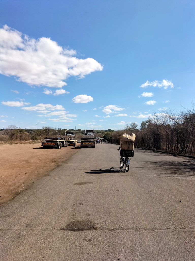 Photo of a large road with some trucks and people walking in the distance.