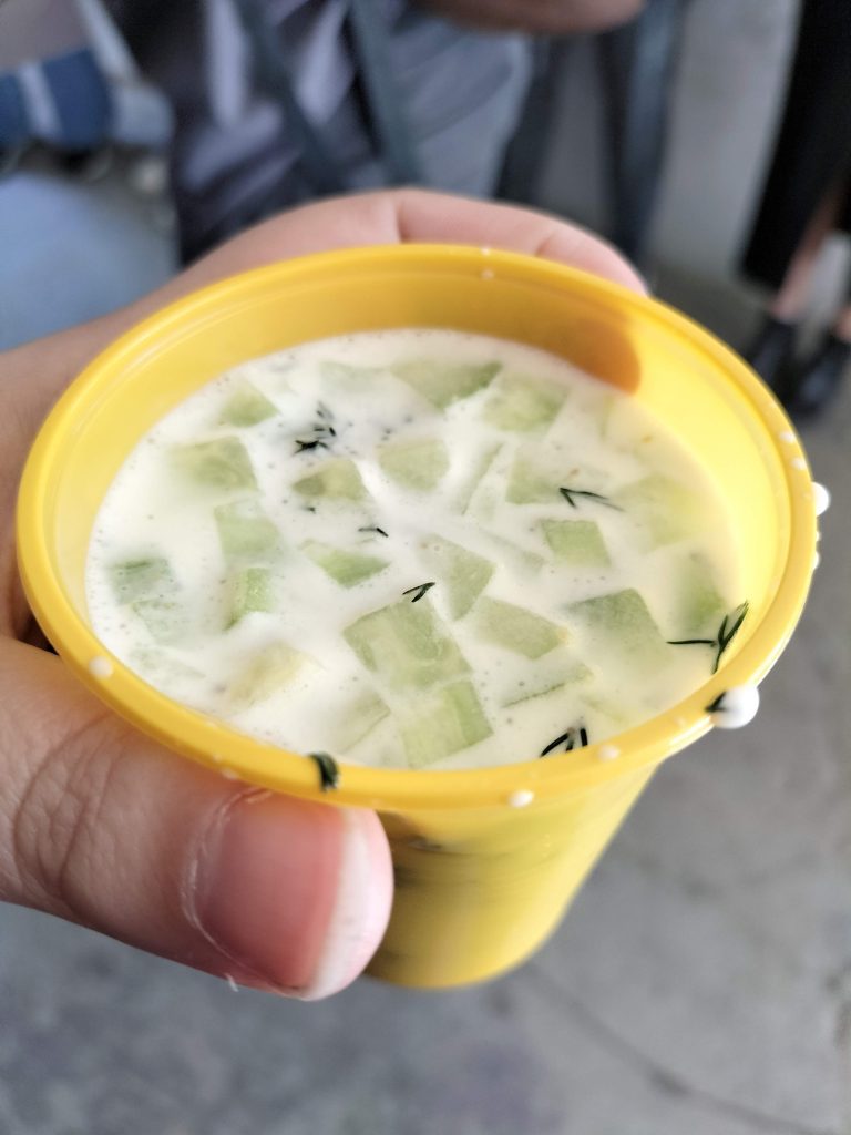 Photo of a cup of soup. It's white with pieces of cucumber floating at the top.