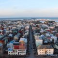 Photo of Reykjavik taken from above. The view shows a main street leading towards the city centre. Cars line the street and many houses are brightly coloured. In the distance you can see the sea with a mountain on the right across the bay.