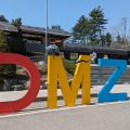 Photo of giant letters outside a building spelling out DMZ. The D is red, M is yellow and Z is blue. A helmet rests on the M and behind it is a flagpole.