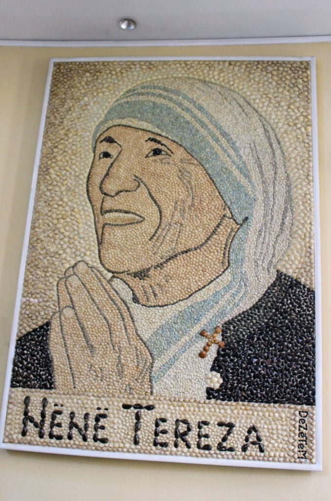 Photo of an image of Mother Teresa's face, with her hands praying. The image is made out of shells of different colours.