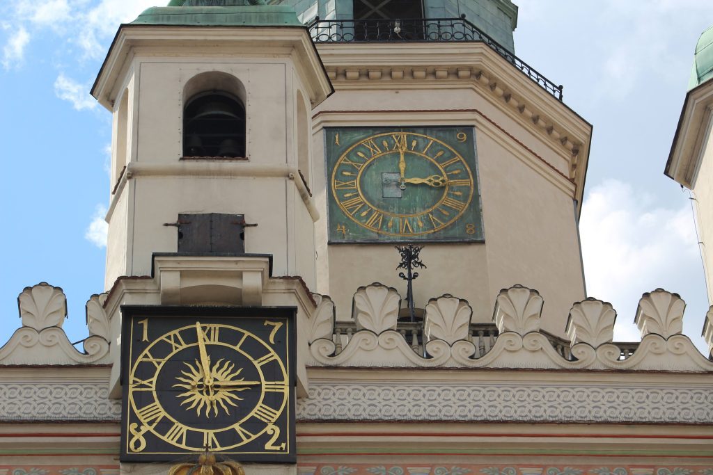 Photo of a black clock with gold roman numerals and hands. The numbers 1782 are on the clock. There is a small platform with two wooden doors above the clock. Behind and to the right is another clock, this time a greenish colour, still with gold detailing and the date 1948.