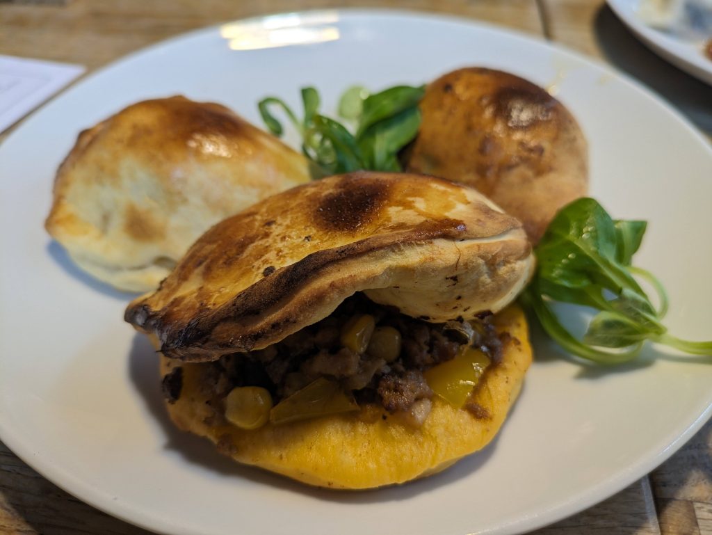 Photo of three baked pierogis sitting on a white place with some green salad between them.