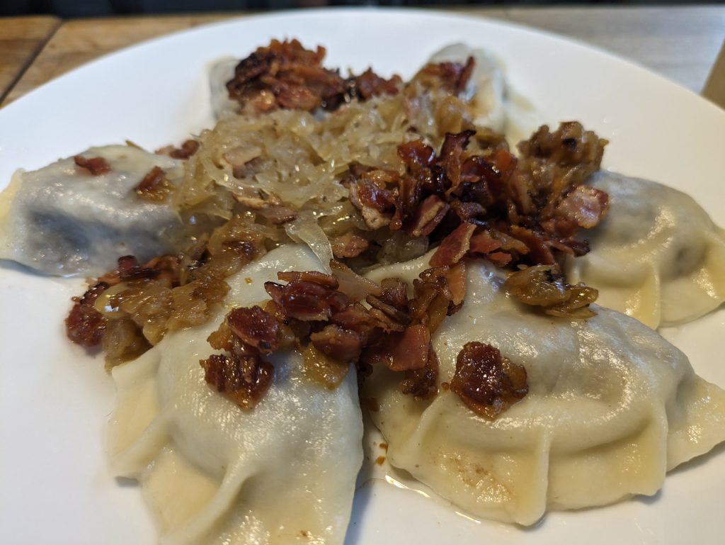 Photo of six boiled pierogis with small bits of crispy bacon on the top along with saurkraut.