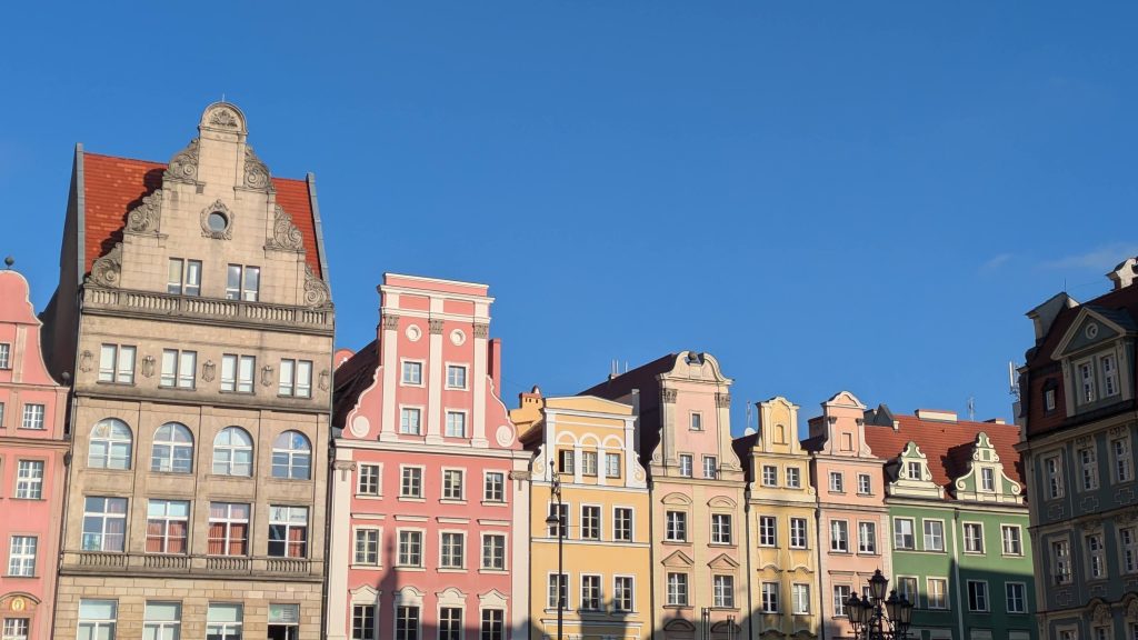 Photo of the tops of bu8ildings in Wroclaw. Each building has a slightly different shape at the top, and they are all painted bright colours.